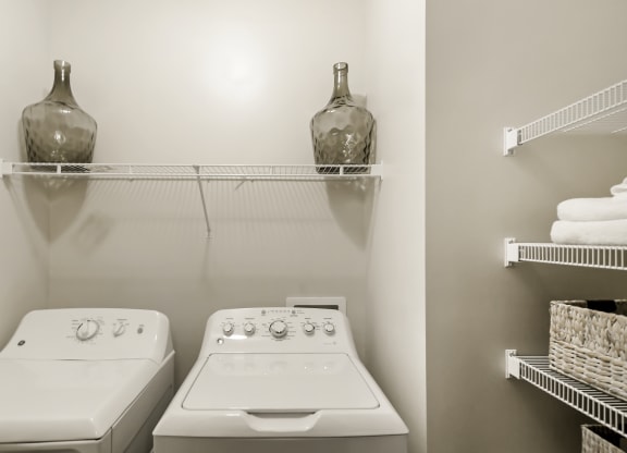 a laundry room with two white appliances and a shelf with a vase on top at Charleston Apartment Homes, Alabama