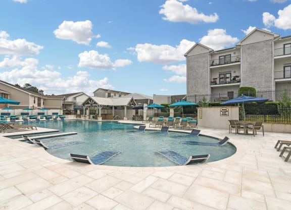 a large pool with lounge chairs and umbrellas in front of an apartment building at Parkwest Apartment Homes, Hattiesburg, MS