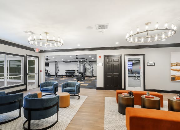a lobby with chairs and tables and a gym in the background at The Woodlands Apartment Homes, Meridian, MS, 39301