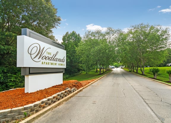 the woodlands sign at the entrance to a road with trees at The Woodlands Apartment Homes, Meridian, Mississippi