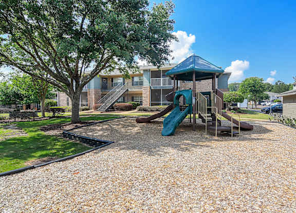 A playground with a slide and a tree in front of a building.