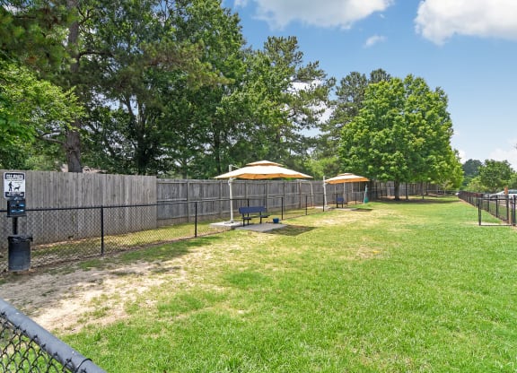 a fenced in dog park with a picnic table and umbrellas at Legacy Apartment Homes in Ridgeland, MS 39157