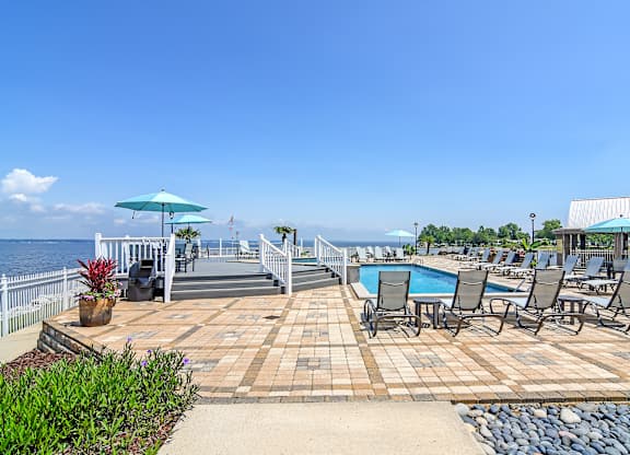 A pool area with chairs and umbrellas overlooking the water at Lakeshore Pointe Apartment Homes, Mississippi, 39047