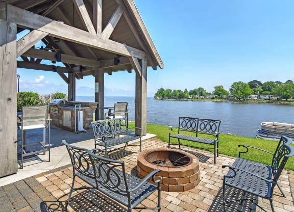 a patio with a fire pit and chairs next to a lake at Lakeshore Pointe Apartment Homes, Brandon, MS