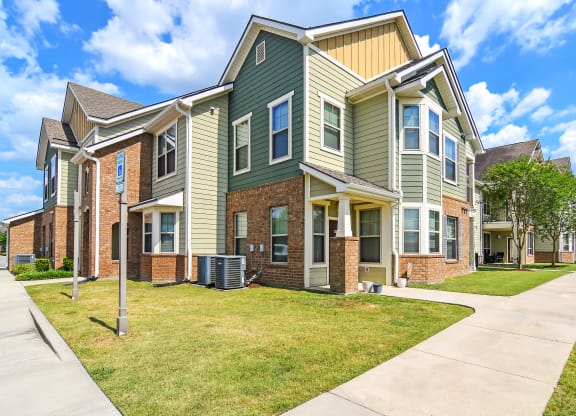 an apartment building with green and brick exterior and a sidewalk at Audubon Park Apartment Homes, Louisiana, 70791