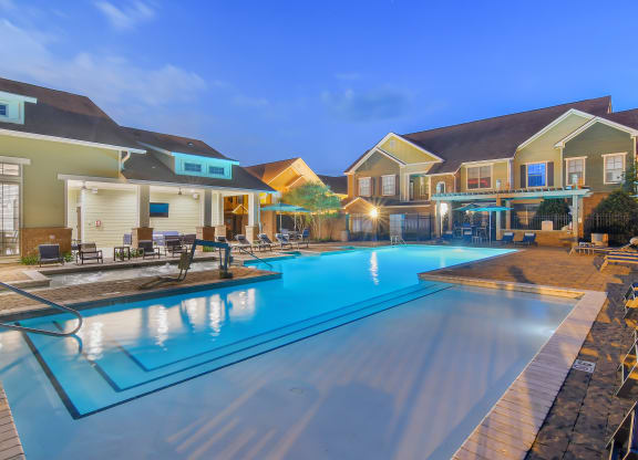 a swimming pool with houses around it at night at Audubon Park Apartment Homes, Zachary, 70791