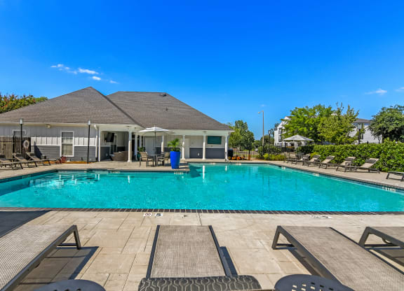a swimming pool with chairs and a house in the background at Avalon Apartment Homes, Starkville, Mississippi