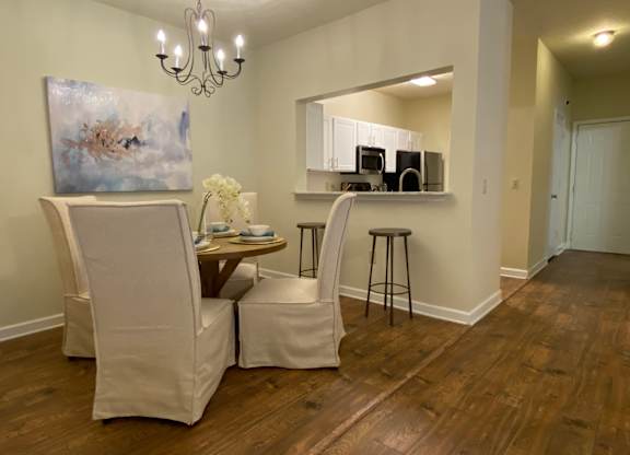 A room with a painting, a chair, a table with a vase of flowers, and a bar area with stools.