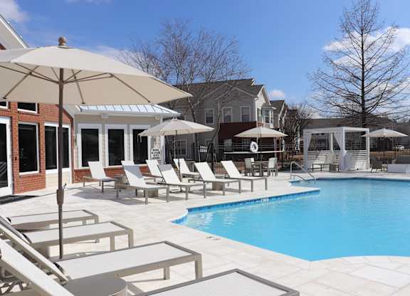 A pool area with a white umbrella and chairs at Carlton Park Apartment Homes in Flowood, MS