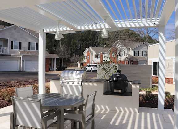 A patio with a table and chairs under a white pergola at Carlton Park Apartment Homes in Flowood, MS