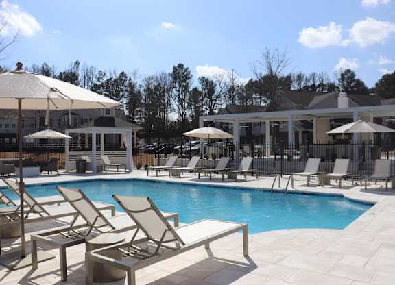 A pool area with sun loungers and umbrellas at Carlton Park Apartment Homes in Flowood, MS