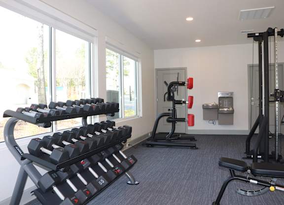 A gym with a row of dumbbells and a bench press at Carlton Park Apartment Homes in Flowood, MS