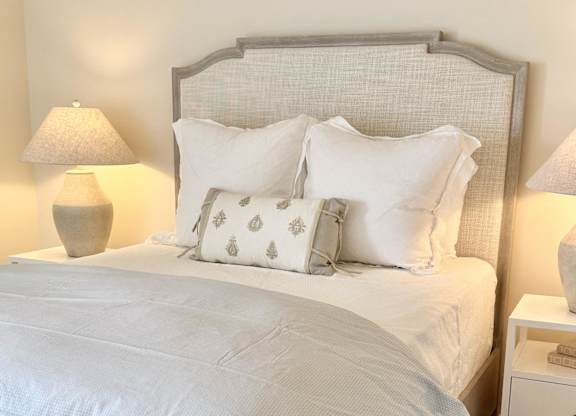 A bed with white bedding and a grey headboard at The Pointe Apartment Homes, MS, 39553