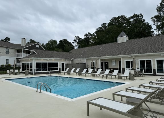 a large swimming pool with lounge chairs in front of a building  at Laurelwood Apartment Homes, Laurel, Mississippi