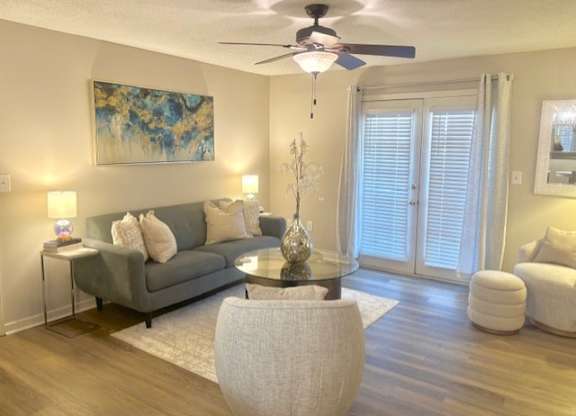 A living room with a grey couch, a glass coffee table, and a ceiling fan.