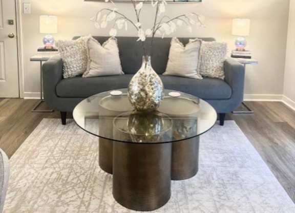 A living room with a grey couch, a glass coffee table, and a painting on the wall.