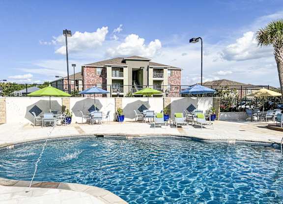 A pool area with a building in the background and lounge chairs around the pool at Canebrake Apartment Homes in Shreveport, LA