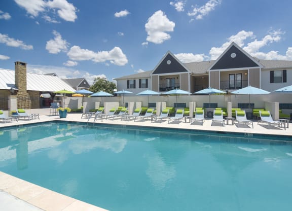 A swimming pool with lounge chairs and umbrellas in front of a building at Reserve of Bossier City Apartment Homes in Bossier City, LA 71111