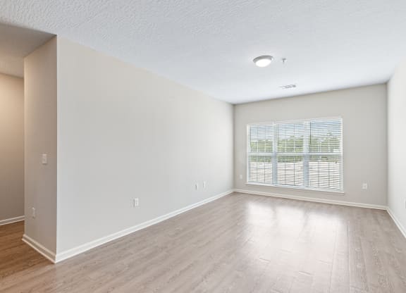 an empty living room with a large window and wood flooring at The Met Apartment Homes, Hattiesburg