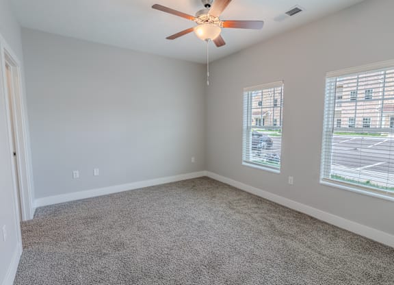an empty living room with two windows and a ceiling fan at The Village at Sandstone Apartments, Greenwood, IN 46142