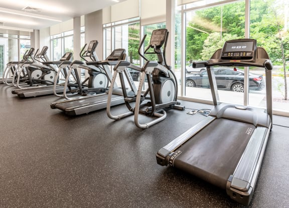 a gym with cardio equipment and large windows