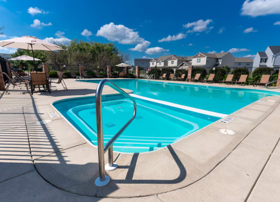 a swimming pool with chairs and umbrellas and houses in the background