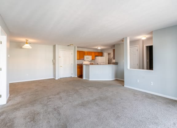 an empty living room with carpet and a kitchen
