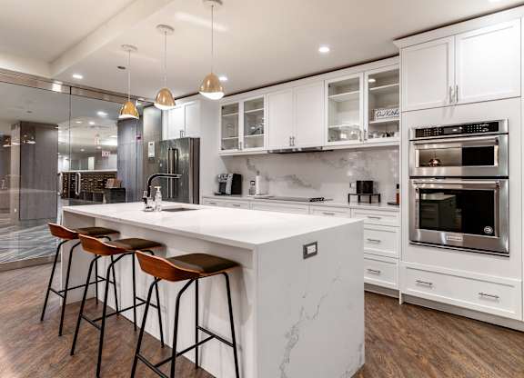 a kitchen with white cabinets and a large island with three stools at Park Heights by the Lake Apartments, Chicago, IL