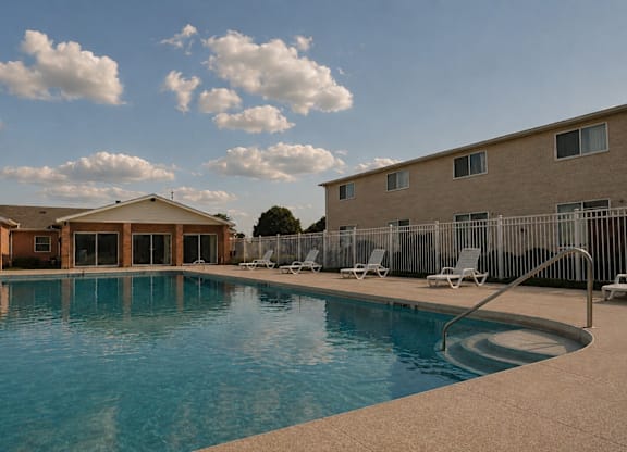 A swimming pool surrounded by chairs and buildings.