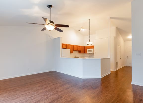 an empty living room with a ceiling fan and a kitchen