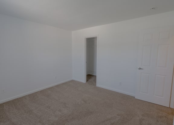 a bedroom with white walls and carpet and a door to a closet