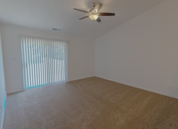 an empty living room with a large window and a ceiling fan