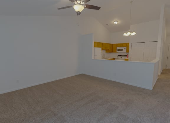 an empty living room with a ceiling fan and a kitchen