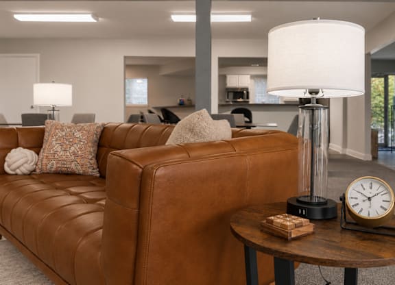 A brown leather couch with a white pillow and a white lamp on a side table.