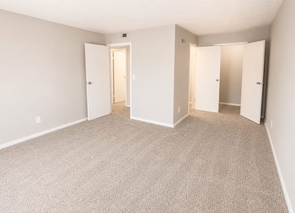 A room with carpeted floor and white walls with three open doors.