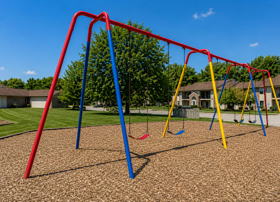 A playground with a red swing set and blue and yellow swings.