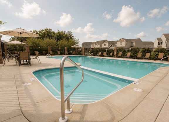 A swimming pool surrounded by a concrete deck and patio furniture.