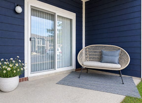 A white chair with a blue cushion is placed on a blue rug in front of a glass door.