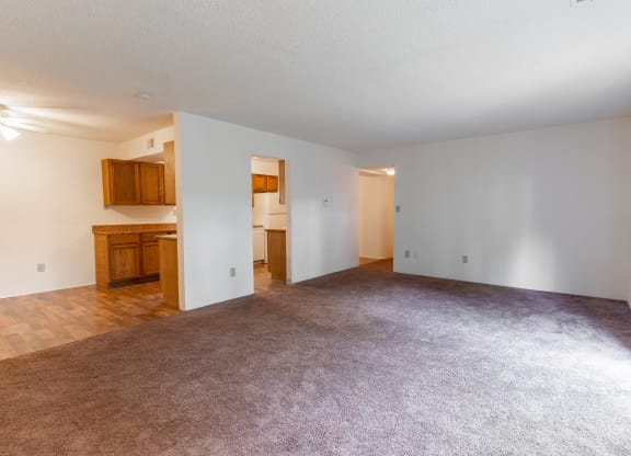 the living room and kitchen of an empty apartment with carpeting and white walls