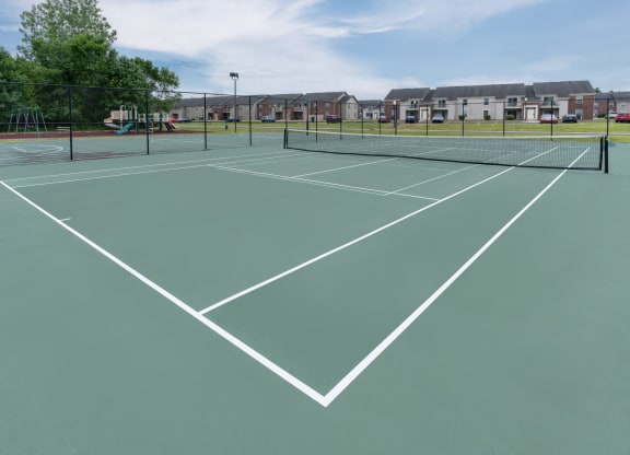 a green tennis court with white lines and houses in the background