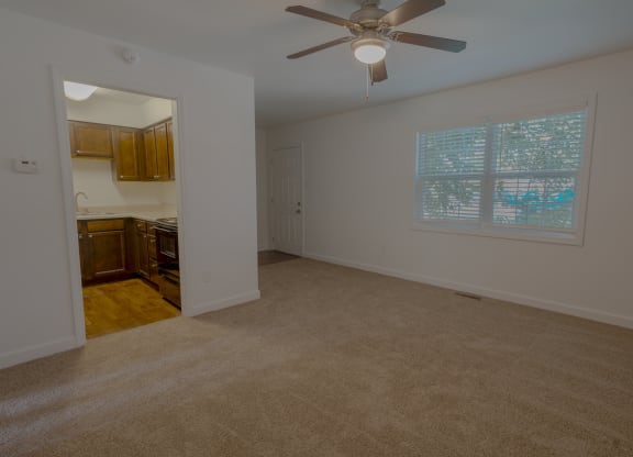 an empty living room with a ceiling fan and a kitchen