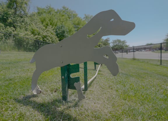 a metal dog statue in the grass near a fence