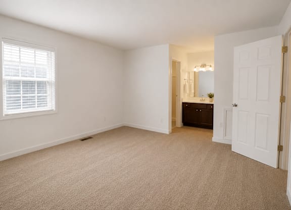 A room with a carpeted floor and a window with blinds.