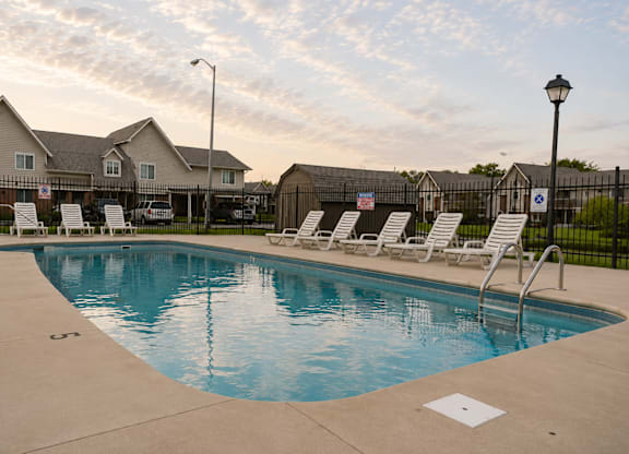 A swimming pool with lounge chairs and a house in the background.