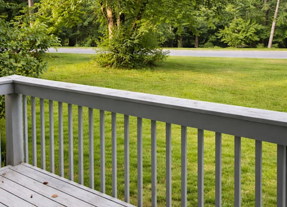 A wooden deck with a white railing overlooks a green lawn.