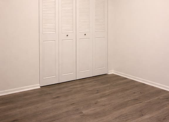 Closed white doors in a room with wooden floors.
