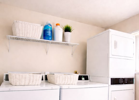 A white kitchen with a white fridge, white cupboards and white baskets.