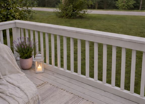 A white railing with a lit candle and a potted plant on a wooden floor.