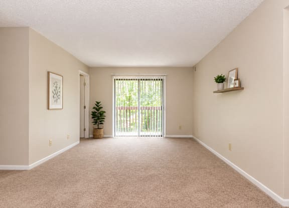 A room with a carpeted floor and a sliding glass door leading to a backyard.