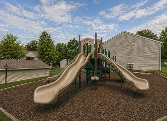 A playground with a green slide and brown ground.